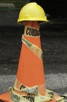 Yellow hardhat on orange traffic cone wrapped with caution (CUIDADO) tape